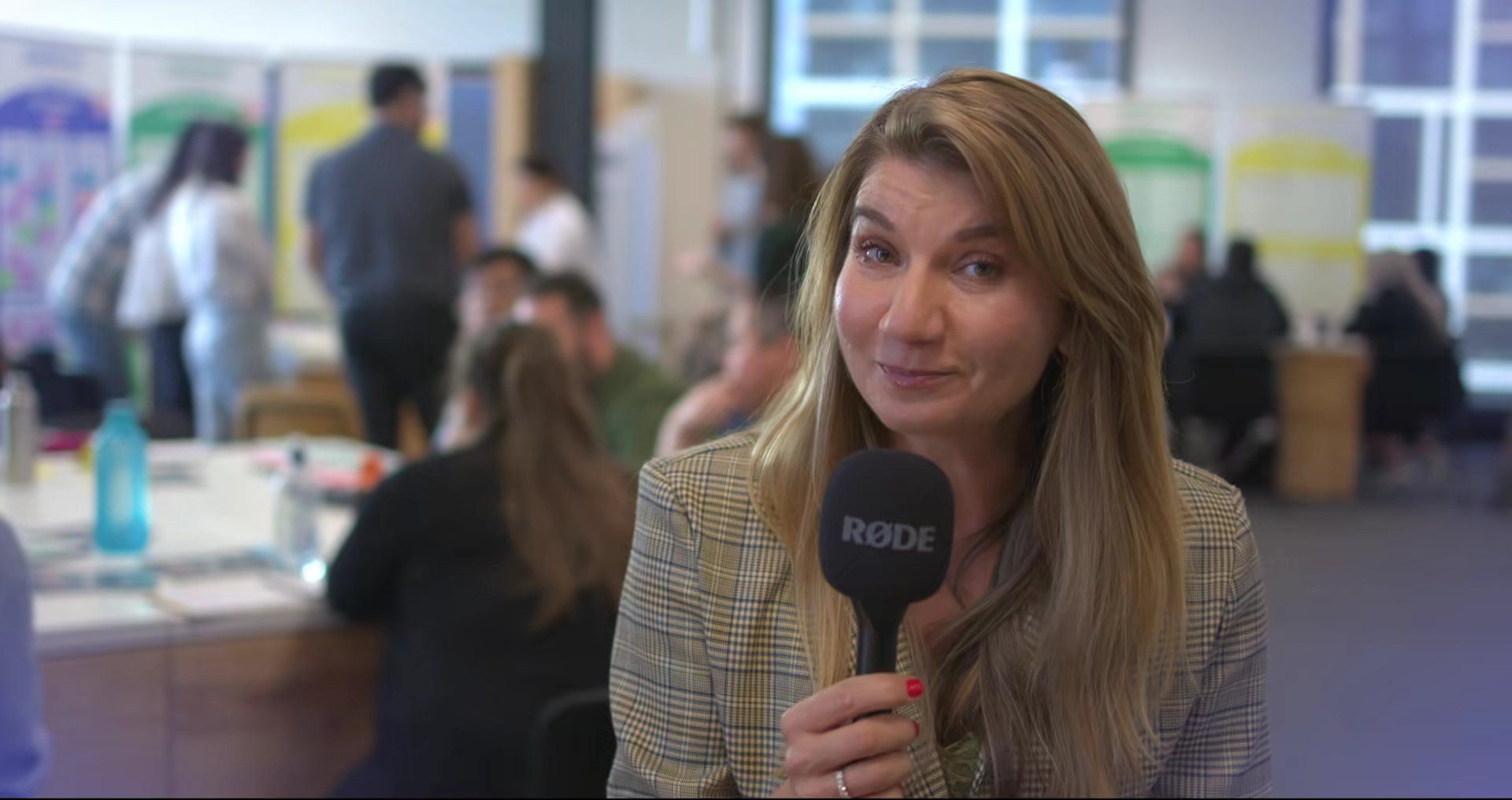 An on-camera interview on the hackathon floor, teams working behind